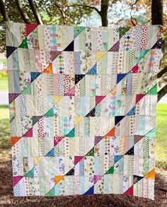 a colorful quilt hanging from the side of a tree in front of some grass and trees