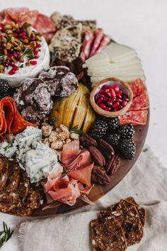 an assortment of meats and cheeses on a wooden platter next to crackers