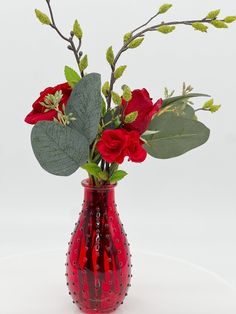 a red vase filled with flowers on top of a white table next to a green leafy branch