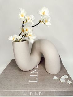 a white vase with flowers in it sitting on top of a book that says linen