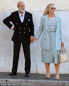 an older man and woman holding hands while standing next to each other on the sidewalk