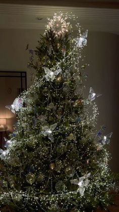 a decorated christmas tree with white lights and butterflies on the top, in a living room