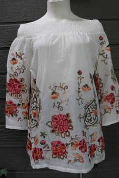 Floral/paisley embroidered blouse with 3/4 length sleeves and a shirred off the shoulder neckline.  100% Cotton Measurements: Small - Bust (armpit to armpit): 38 inches - Waist: 39 inches - Sleeve Length: 19 inches - Total Length (shoulder to bottom hem): 27 inches Medium - Bust (armpit to armpit): 42 inches - Waist: 43 inches - Sleeve Length: 19 inches - Total Length (shoulder to bottom hem): 28 inches Bohemian Blouse With Elastic Neckline For Spring, Bohemian Long Sleeve Off-shoulder Top, Bohemian Tops With Elastic Neckline For Spring, White Embroidered Off-shoulder Top, Fitted Bohemian Off-shoulder Top For Spring, Spring Peasant Top With 3/4 Sleeves, Peasant Style 3/4 Sleeve Spring Tops, Summer Long Sleeve Tops With Elastic Neckline, Peasant Style 3/4 Sleeve Tops For Spring