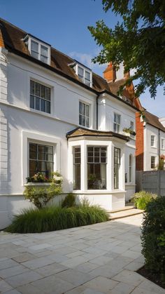 a large white house with lots of windows and plants in the front garden area on a sunny day