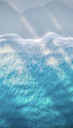 an aerial view of the ocean with waves and mountains in the backgroung