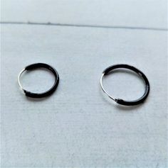 Black Hoop Earrings made by Silver Sterling 925. You can choose Size: - 10mm diameter x 1,2mm - 12mm diameter x 1,2mm - 14mm diameter x 1,2mm The black color is achieved by enameling silver with Ruthenium. In the seafaring tradition, the number of rings a sailor wore indicated the voyages he had completed. 1 hoop Cape Horn, 2 Cape of Good Hope, 3 Hoops around the world. Our earrings are sent in wooden boxes silk-screened by us, the boxes are made of recycled wood from the North of Galicia (Spain Black Minimalist Sterling Silver Cartilage Earrings, Black Single Huggie Earring As A Gift, Minimalist Black Small Hoop Huggie Earrings, Black Minimalist Pierced Hoop Earrings, Minimalist Black Round Cartilage Earrings, Black Sterling Silver Hoop Earrings For Everyday, Minimalist Black Hoop Cartilage Earrings, Everyday Black Sterling Silver Hoop Earrings, Black Round Cartilage Earrings For Everyday Wear