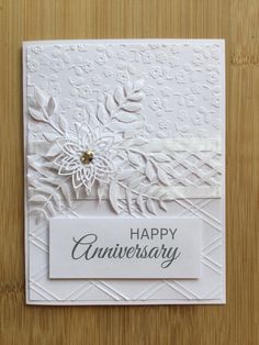 an anniversary card with white paper flowers and leaves on it, sitting on a wooden surface