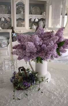 a white vase filled with purple flowers on top of a table