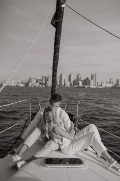 a man and woman sitting on the back of a sailboat in front of a city skyline