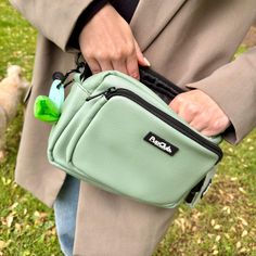 a person holding a small green bag in their hand and a dog walking behind them