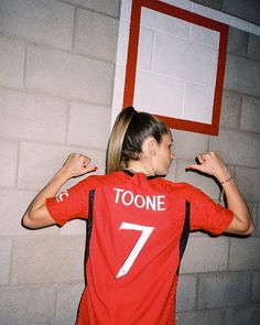 a woman in a red shirt holding a white frisbee near a brick wall