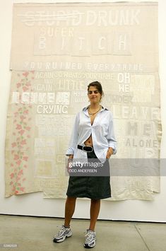 a woman standing in front of a wall with words on it and an art piece behind her