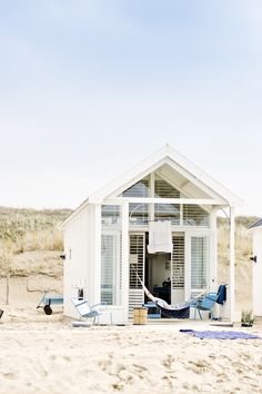 a small white building sitting on top of a beach next to a blue chair and umbrella