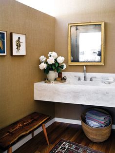 a bathroom sink sitting under a mirror next to a wooden bench with flowers on it