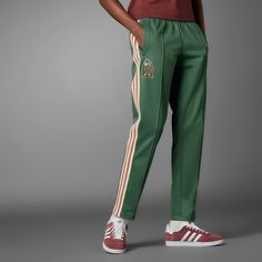 a man wearing green sweatpants with red and white stripes on the side, standing in front of a gray background