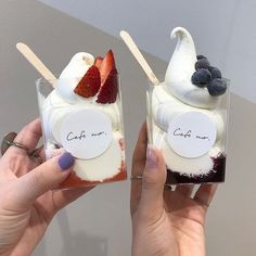 two people holding up small desserts with strawberries and blueberries on each one