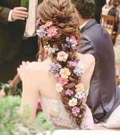 a woman with flowers in her hair sitting at a table next to a man wearing a suit