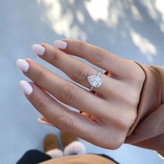 a woman's hand with a diamond ring on her left hand and white nails