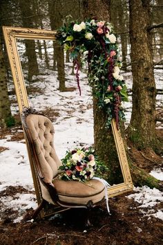 an old chair sitting in the snow next to a tree with a mirror on it