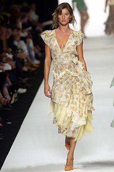 a woman walking down a runway wearing a dress with ruffles on the skirt