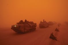 several tanks driving down a dusty road in the middle of an orange foggy day