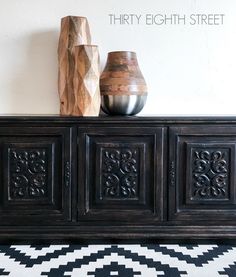 two vases sitting on top of a black and white rug next to a wooden cabinet