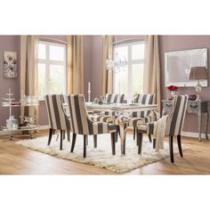 a dining room table with striped chairs and rug on the floor in front of two windows