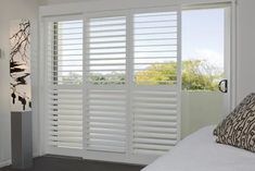 a white bed sitting next to a window with shutters on the side of it