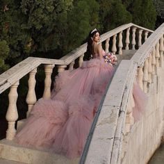 a woman in a pink dress is sitting on the stairs with her hands behind her back