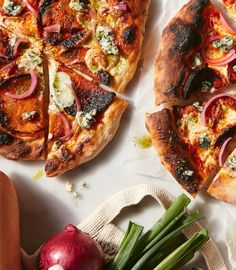 two pizzas sitting on top of a table next to onions and radishes