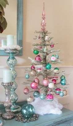 a small christmas tree with ornaments and candles on a blue table in front of a mirror