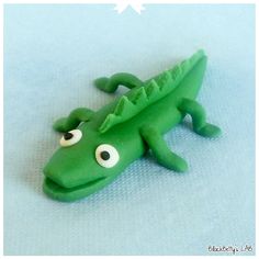 a green toy alligator with googly eyes on it's head and tail, sitting on a blue surface