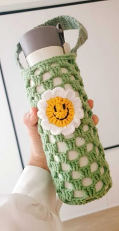 a woman holding up a green crocheted water bottle with a smiling face on it