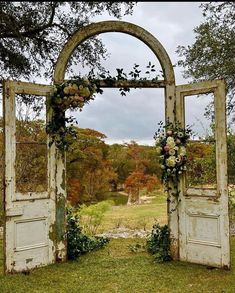 an old door is decorated with flowers and greenery in front of a grassy field