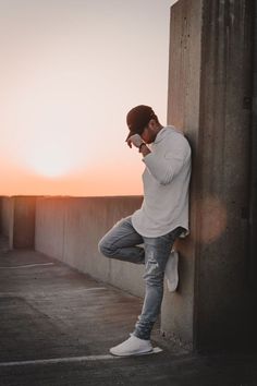 a man leaning against a wall and looking at his cell phone as the sun sets