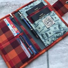 an orange and red checkered wallet with a passport, money, and pen