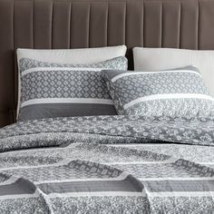 a bed with grey and white comforter on it's headboard next to pillows