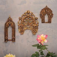 three ornate gold wall hangings and a pink rose