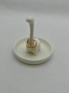 a white ring holder with a gold and diamond ring on it