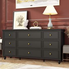 a black dresser with gold knobs in a living room next to a painting and lamp