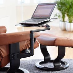 a laptop computer sitting on top of a leather chair next to a footstool