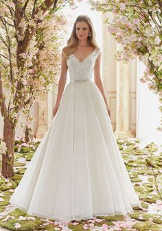 a woman in a white wedding dress standing on a path with flowers and trees around her