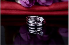 two wedding rings sitting next to each other on top of a table with flowers in the background