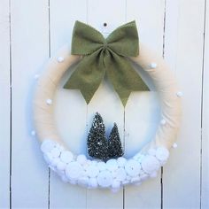 a wreath decorated with white balls and green bow hanging on the wall next to a pair of black shoes