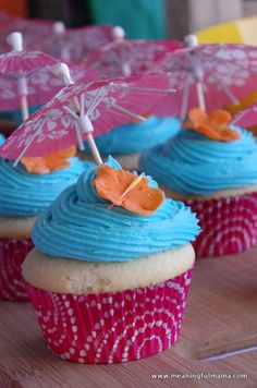 cupcakes with blue frosting and pink umbrellas on top are sitting on a table