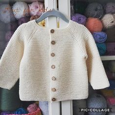 a white knitted sweater hanging on a rack with balls of yarn in the background