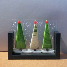 three small green and white christmas trees in a black frame on a table top with snow around them