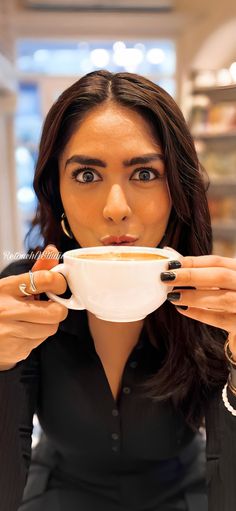 a woman holding a bowl of soup in front of her face and looking at the camera