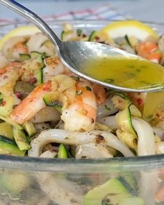 a glass bowl filled with shrimp, zucchini and lemon wedges next to a spoon