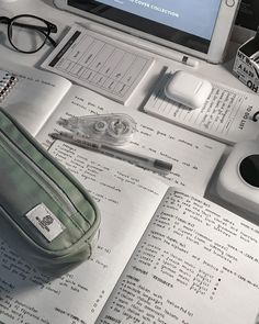 a laptop computer sitting on top of a desk next to an open book and pen